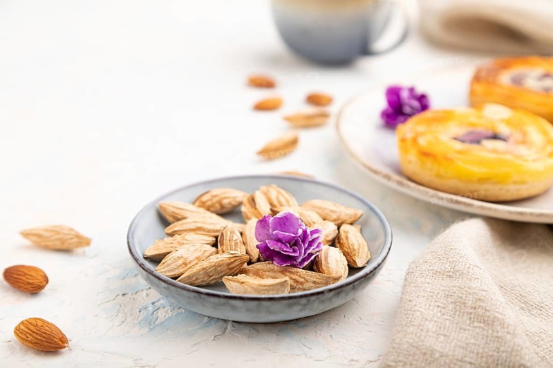 Small cheesecakes with jam and almonds with cup of coffee on a white concrete background and linen textile. Side view, close up, selective focus