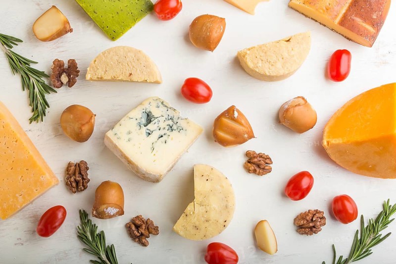 Set of different types of cheese with rosemary and tomatoes on a white wooden background. Top view, flat lay, close up