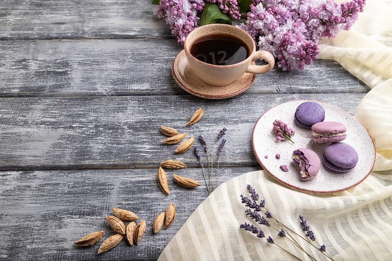 Purple macarons or macaroons cakes with cup of coffee on a gray wooden background and white linen textile. Side view, copy space