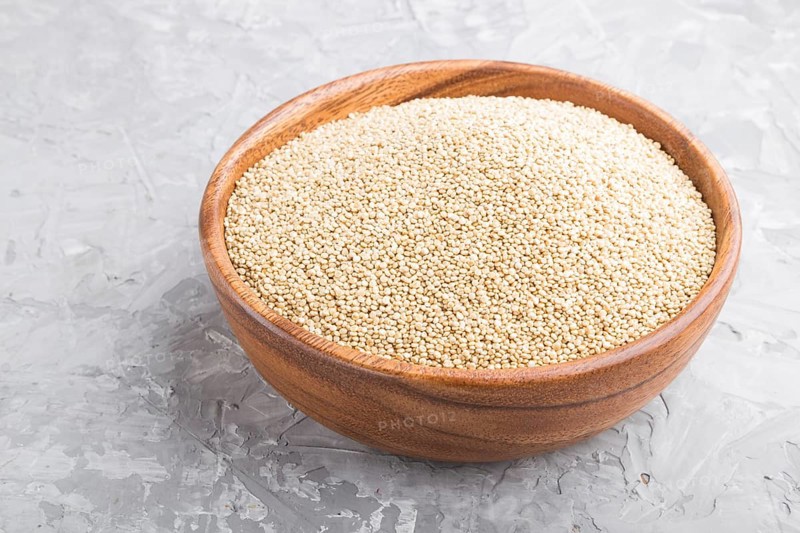 Wooden bowl with raw white quinoa seeds on a gray concrete background. Side view, close up