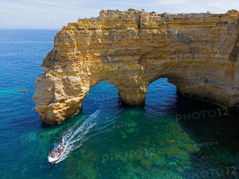 A large boat passes under natural arches made of rocks in crystal clear water on the coast, aerial view, Praia da Marinha, double rock arch, Lagoa, Rocky Algarve, Algarve, Portugal, Europe