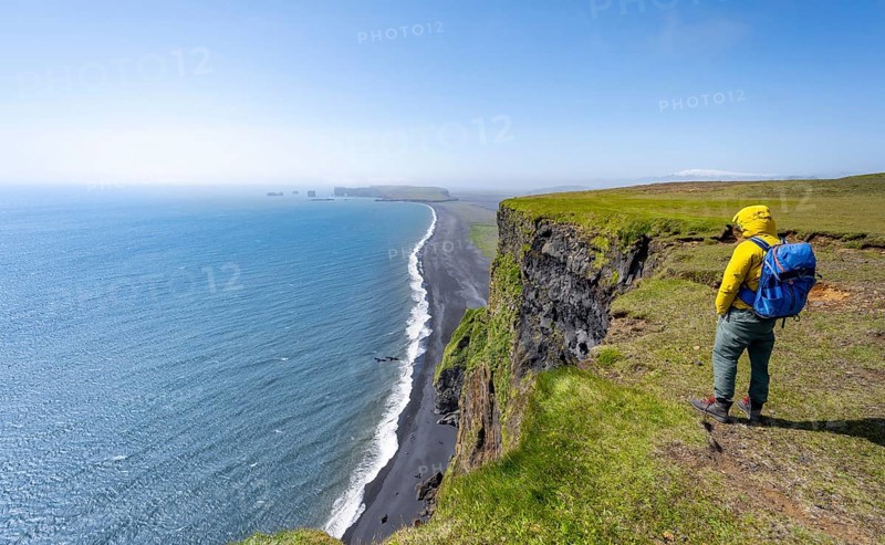 Young man standing on cliff, view from steep cliff over Reynisfjara beach, Black sand beach, Vik, South Iceland, Iceland, Europe
