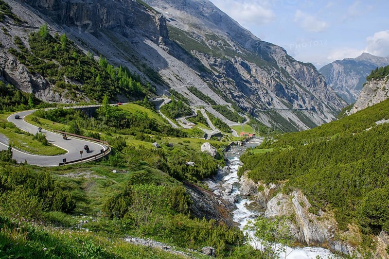 View to the south in Braulio valley with in front right water from Cascata del Braulio waterfall flowing on in the background to E-Werk electricity plant hydroelectric power plant power station Centrale Idroelettrica A2A del Braulio for power generation production of electricity from hydropower, left pass road south ramp ascent to Umbrail Pass and Stelvio Pass Stelvio, Bormio, Lombardy, Italy, Europe