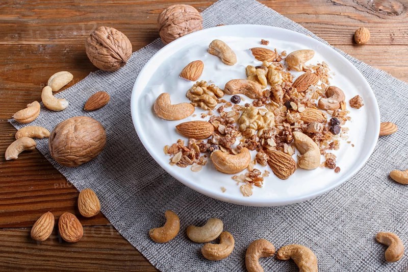 White plate with greek yogurt granola, almond, cashew, walnuts on brown wooden background. close up. copy space
