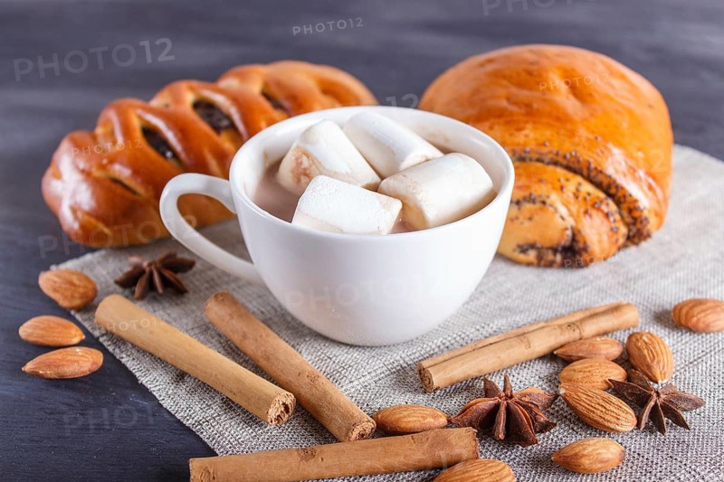 A cup of hot chocolate with marshmallow, buns and spices on linen napkin and black wooden background. close up, copy space