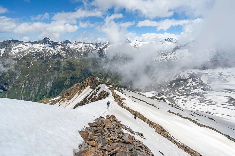 Mountaineer on a rocky ridge with snow, descent from the summit of Schönbichler Horn, view of snow-covered mountain peaks and valley Zemmgrund, Berliner Höhenweg, Zillertal Alps, Tyrol, Austria, Europe