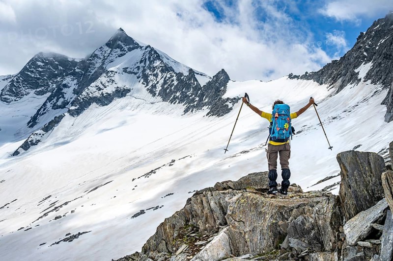 Mountaineer on a rock between snow, raises her arms triumphantly, descending from the summit of Schönbichler Horn, view of snow-covered and glaciated mountain landscape with summit GroÃŸer Möseler, Berliner Höhenweg, Zillertal Alps, Tyrol, Austria, Europe