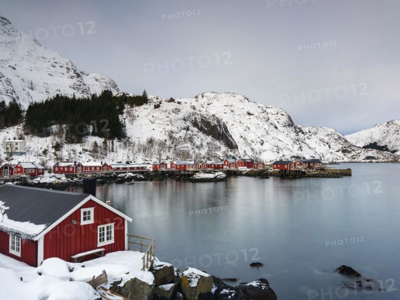 Traditional red rorbu houses on stilts in the authentic fishing village of Nusfjord, snow-capped mountains in the background, Flakstadoya, Lofoten, Norway, Europe