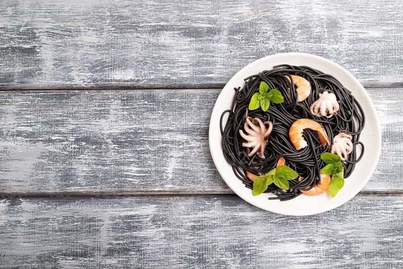 Black cuttlefish ink pasta with shrimps or prawns and small octopuses on gray wooden background. Top view, flat lay, copy space