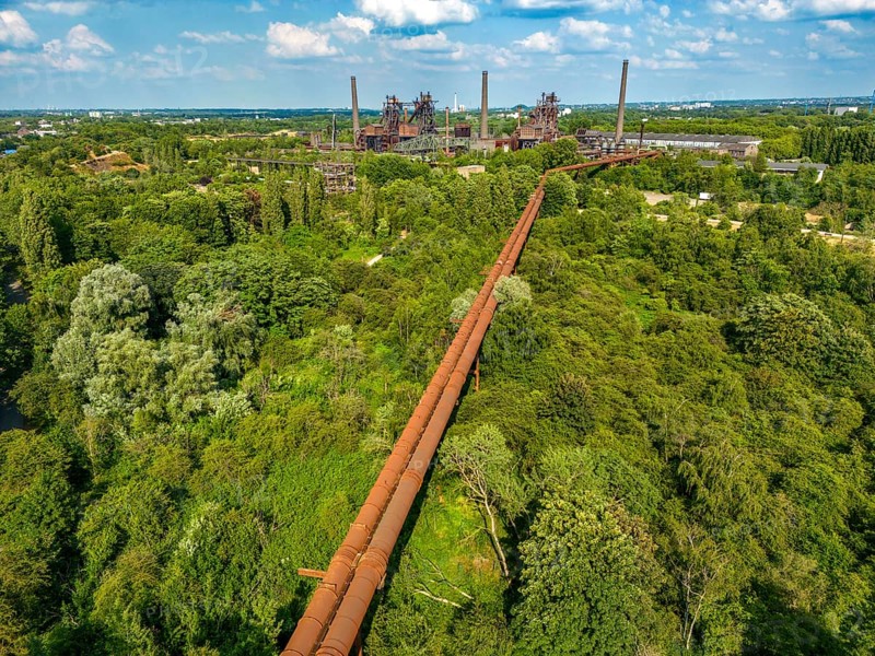 The Duisburg Nord Landscape Park, double blast furnace gas pipeline from the west View across the wilderness, a park area where nature is left to its own devices, to the steelworks, North Rhine-Westphalia, Germany, Europe