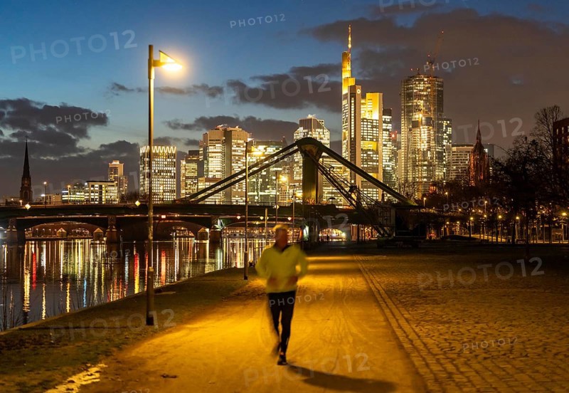 Skyline of the city centre of Frankfurt am Main, joggers on the pavement, promenade along the river Main, dusk, Hesse, Germany raft bridge in the background