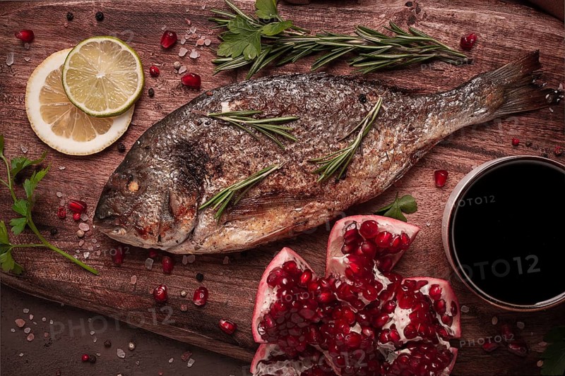 Fried dorado fish, with spices and herbs, on a wooden board, pomegranate sauce, close-up, no people