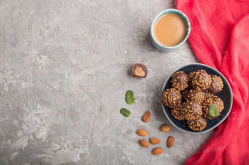 Chocolate caramel ball candies with almonds and a cup of coffee on a gray concrete background and red textile. top view, flat lay, copy space