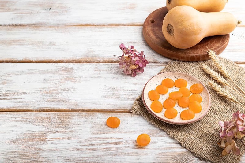 Jelly pumpkin candies on white wooden background and linen textile. copy space, side view. autumn concept