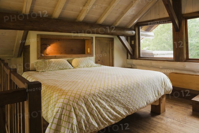 King size bed with wood frame in sparsely furnished Zen style master bedroom on mezzanine inside Scandinavian hybrid style log cabin home, Quebec, Canada, North America