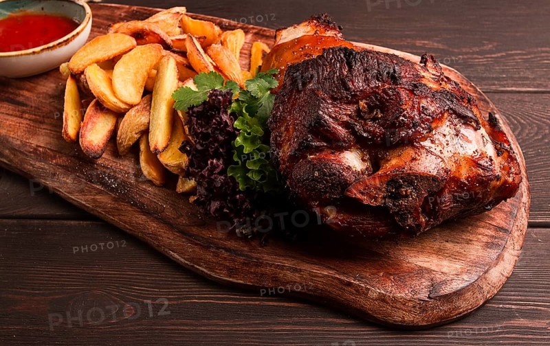 Pork knuckle, in soy-honey sauce, with fried potatoes, on a wooden chopping board, homemade, no people