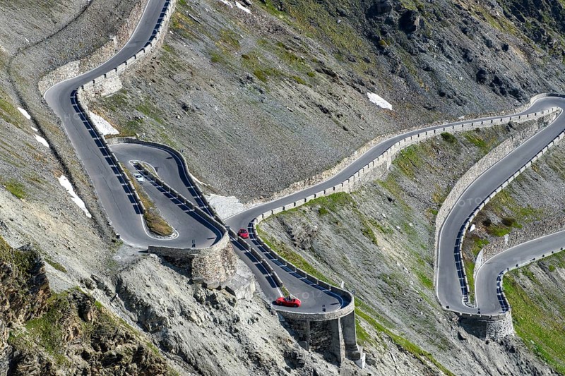 View from an elevated position from a bird's eye view like an aerial view of three hairpin bends in direct succession serpentines steep narrow bend bends above tree line from driveway on in steep slope steep slope built to from 2757 2758 metres high pass high pass road mountain pass alpine pass Stelvio Stelvio Pass, in the middle lower half of the picture two red sports cars Porsche, Stelvio, South Tyrol, Alto Adige, Italy, Europe