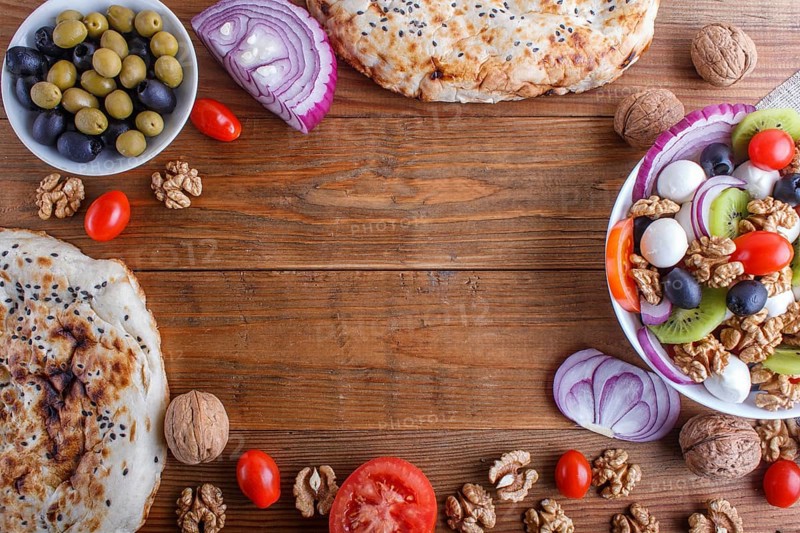 Frame made from cherry tomatoes, mozzarella cheese, olives, kiwi, onion and walnuts on brown wooden background, copy space, top view