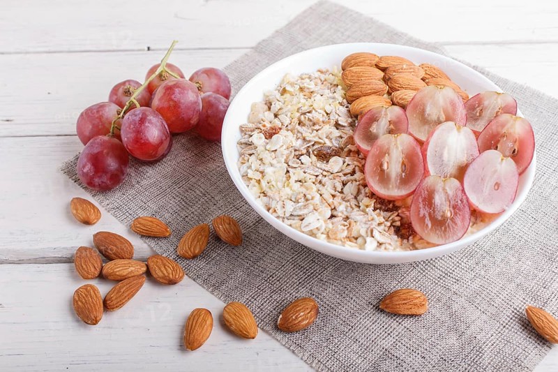 A plate with muesli, almonds, pink grapes on a white wooden background. close up