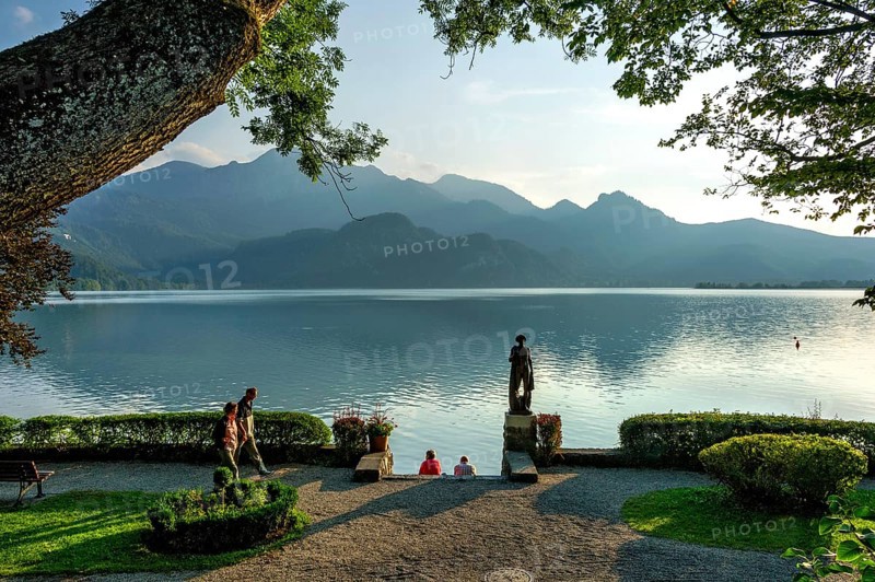 Strollers in the evening light, lakeside promenade with the fisherman statue by Richard Miller, replica, Kochel am See, Lake Kochel, mountains Herzogstand, Rötelstein, Heimgarten, Bavarian Alpine foothills, Alps, Upper Bavaria, Bavaria, Germany, Europe