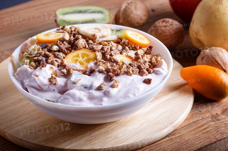 Vegetarian salad of bananas, apples, pears, kumquats, kiwi with granola and yogurt on brown woodem background, close up, selective focus