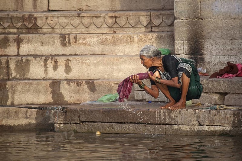 Old washerwoman washing linen in polluted water of the Ganges river at Varanasi, Uttar Pradesh, India, Asia