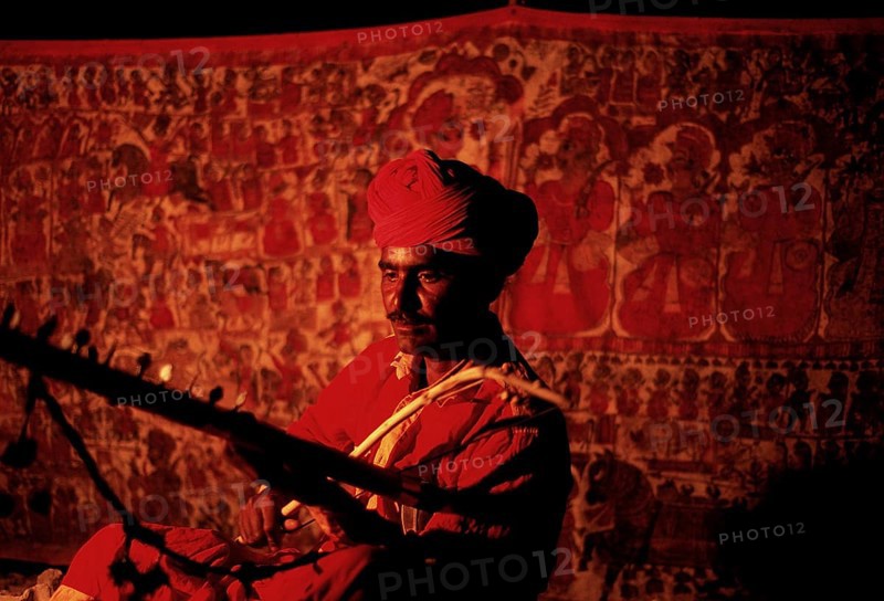 Hindu man playing music, Pabuji bhopa playing ravanhatha, Rajasthan, India. The Bhopa caste is a community of priests-singers of folk deities in western India. The man is honouring Pabuji, a local god in Rajasthan. The scroll behind the man is depicting the life of Pabuji. The ravanhatta is an ancient stringed instrument that could be the ancestor of the violin. Despite being priests, they have a low status in the hindu caste system because folk deities are not brahmanical gods