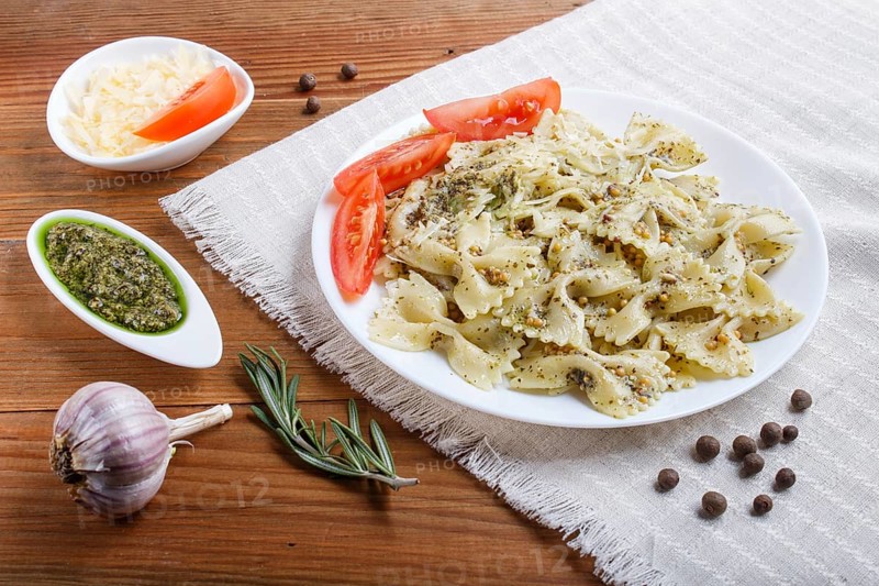 Farfalle pasta with pesto sauce, tomatoes and cheese on a linen tablecloth on brown wooden background. close up
