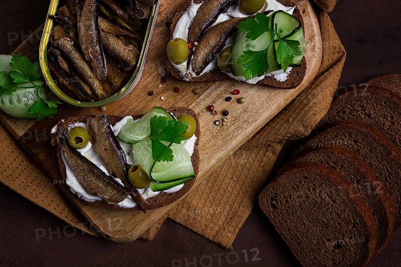 Sandwiches, black bread with sprats, cream cheese, cucumbers, on a cutting board, top view, close-up, no people