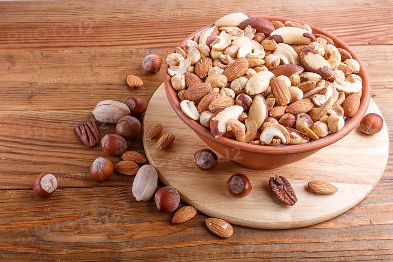 Mixed different kinds of nuts in ceramic bowl on brown wooden background with copy space. hazelnut, brazil nut, almond, pumpkin seeds, cashew. top view