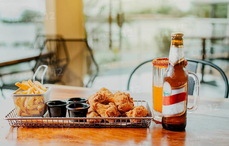 Traditional spicy chicken wings with fries and michelada accompanied with beer served on wooden table