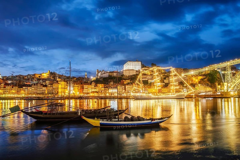 View of Porto city and Douro river with traditional boats with port wine barrels and sailing ship from famous tourist viewpoint Marginal de Gaia riverfront in night. Porto, Vila Nova de Gaia, Portugal, Europe