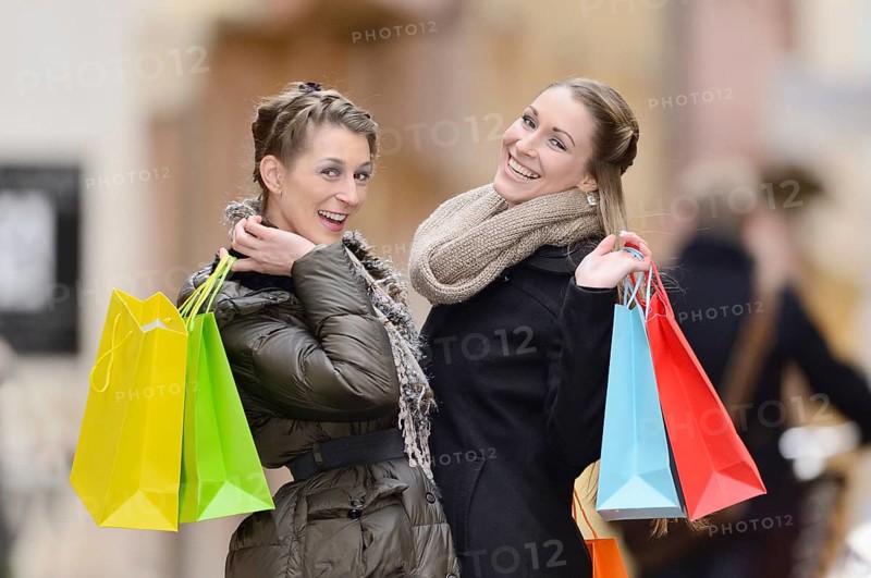 Two joyful women holding colorful shopping bags, posing outdoors in winter attire, Regensburg, Bavaria
