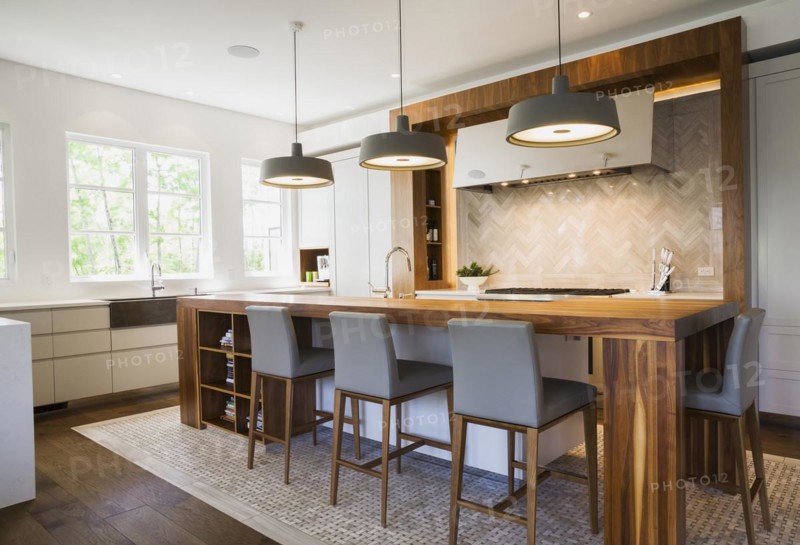 Walnut wood island with grey leather and wooden high chairs on travertine mosaic floor surrounded by engineered hickory wood floorboards in kitchen inside a luxurious contemporary bungalow style home, Quebec, Canada, North America