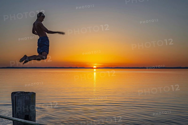 Boy jumping from the wooden jetty into the water at sunset, Chieming, Chiemsee, Chiemgau, Bavaria, Germany Europe