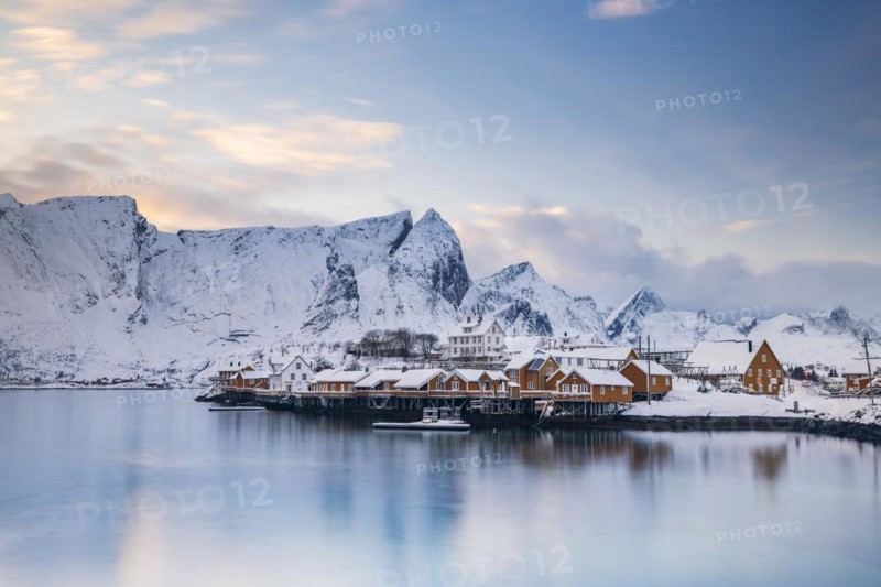 Traditional yellow rorbuer huts on the island of Sakrisoy, snow-capped mountains in the background, Sakrisoy, Reine, Lofoten, Norway, Europe