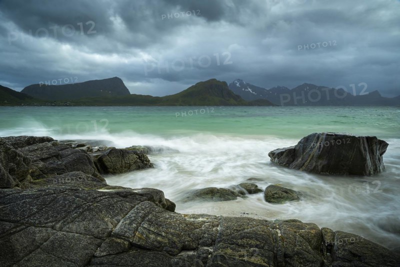 Seascape on the beach at Haukland. View of the mountains of Vestvagoya and Myrland on Flakstadoya. Offersoykammen on the left. Clouds in the sky. Rocks in the foreground. Early summer. Long exposure. Haukland Beach, Haukland, Vestvagoya, Lofoten, Norway, Europe