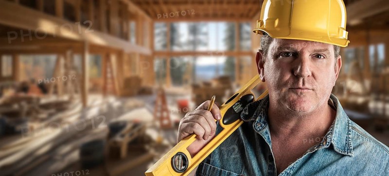 Hard working male contractor at a construction site wearing a hard hat and work gloves holding his level