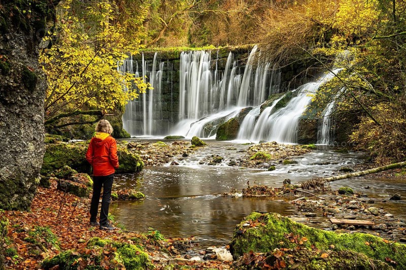 The Geratser waterfall in autumn. A hiker stands on the bank. Moss-covered rocks and trees in autumn leaves. Gerats, Upper AllgÃ¤u, AllgÃ¤u, Bavaria, Germany, Europe