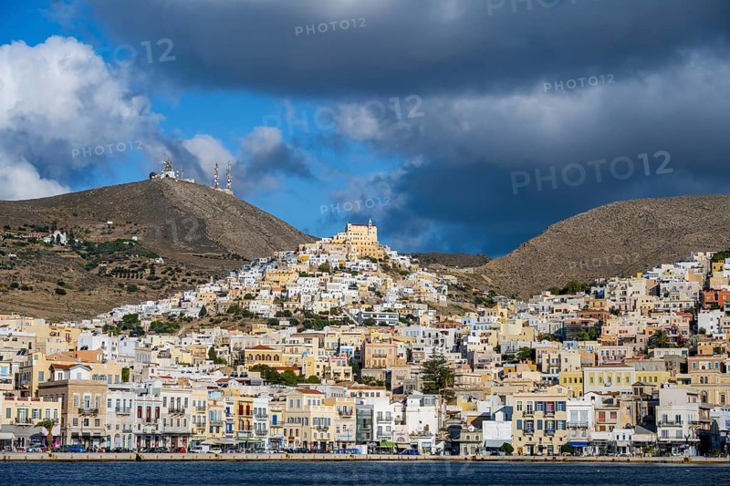 View of the town of Ermoupoli with pastel-coloured houses and sea, on the hill Basilica of San Giorgio in Ano Syros, dramatic cloudy sky, Ermoupoli, Syros, Cyclades, Greece, Europe