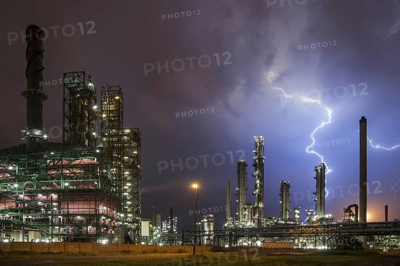 Lightning bolts striking over oil refinery at industrial estate during heavy thunderstorm at night, conceptual picture for global warming due to carbon dioxide emissions