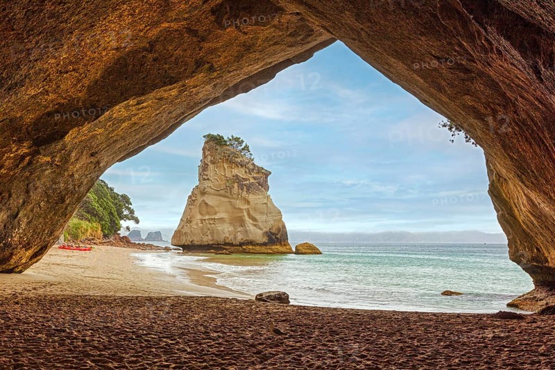 View through a rock arch onto a sandy beach and the sea with gentle waves, Cathedral Grove, Coromandel, New Zealand, Oceania