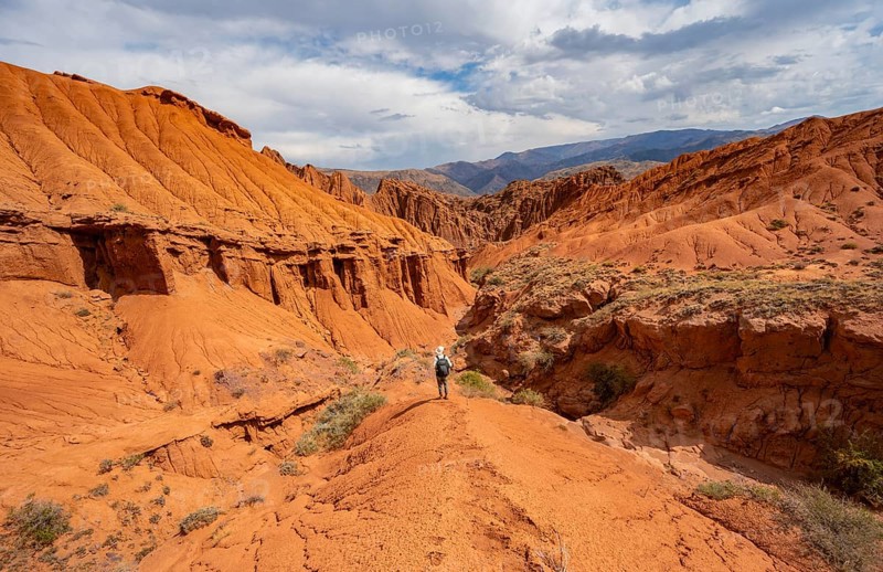 Mountaineer on a mountain ridge, view of eroded mountain landscape with sandstone cliffs, canyon with red and orange rock formations, Konorchek Canyon, Chuy, Kyrgyzstan, Asia