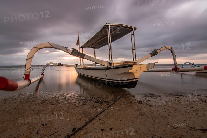 Jukung in the sea, typical landscape shot with a view of the horizon over the water, taken from a sandy beach. Traditional fishing boat at sunrise. Landscape shot of Sanur, Bali, Indonesia, Asia