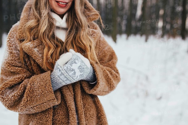 Young woman in fur coat, gloves and scarf in snowy forest.
