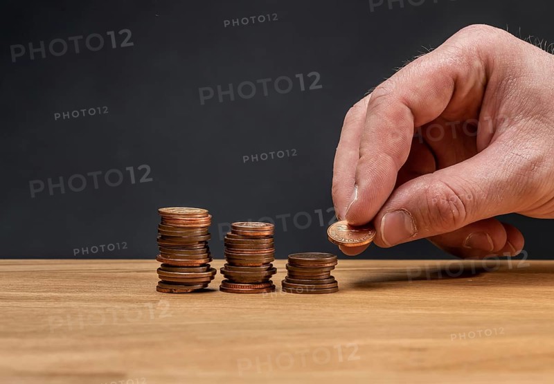 A hand stacking coins on a wooden table against a dark background