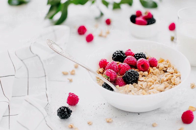 Morning healthy breakfast, white bowl full with granola, muesli, raspberry, blackberry on gray concrete table. Healthy eating, eco, bio food concept. Fresh tasty meal on grey background. Quality photo