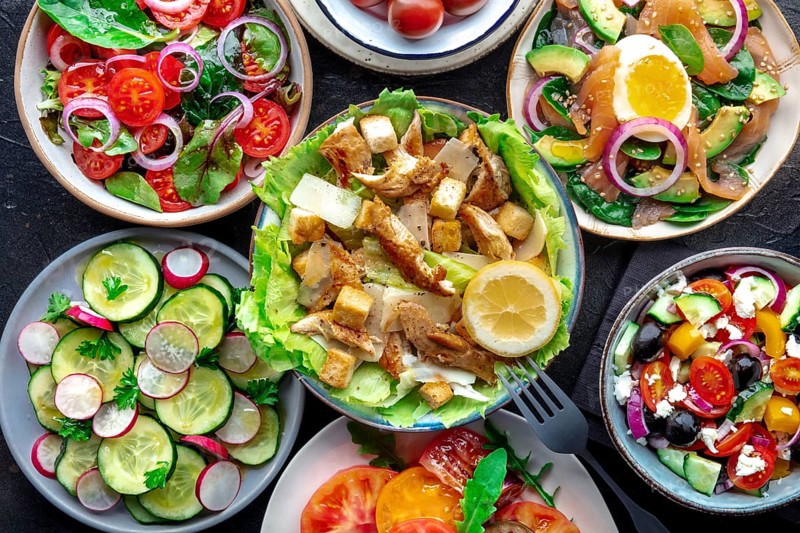 Fresh salads, overhead flat lay shot of an assortment. Variety of plates and bowls with green vegetables. Healthy food. Chicken Caesar salad, salmon and avocado, tomatoes etc, Food photography