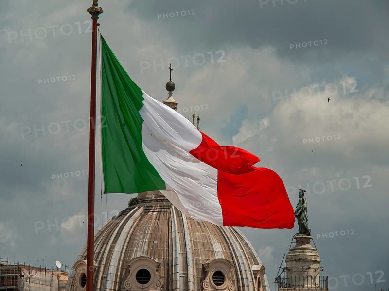 The Italian flag flies in front of a dome and a sculpture under a cloudy sky, rome, italy