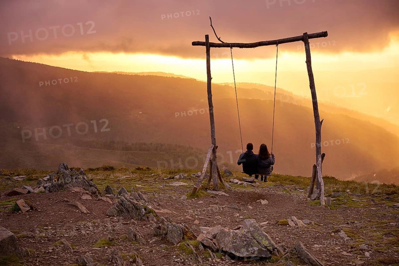 Romantic couple social distancing swinging on a Swing baloico in Lousa mountain, Portugal at sunset